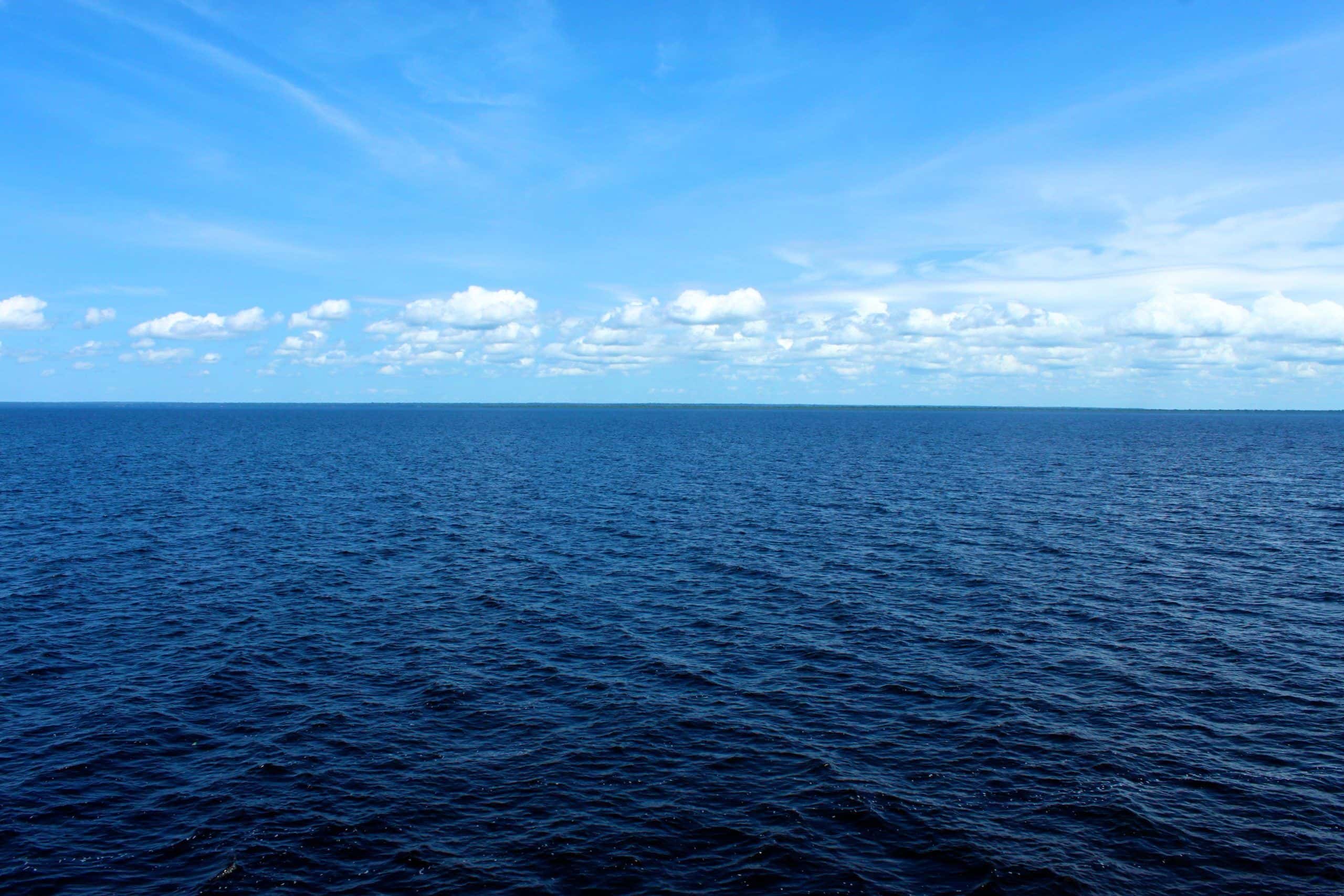 Foto de un mar en calma bajo un cielo azul con nubes en el fondo